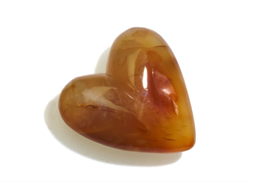 A carnelian gemstone hand-carved into the shape of a heart on a white background.