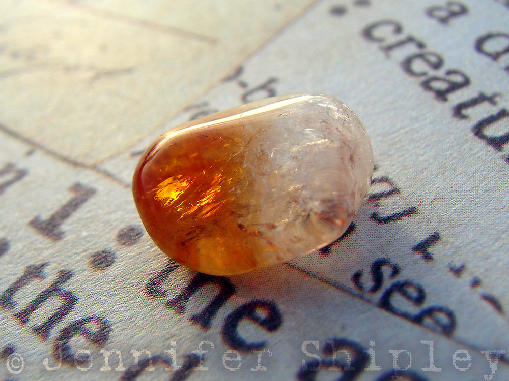 An orange and white tumbled heat-treated amethyst citrine sitting on neutral scrapbook paper