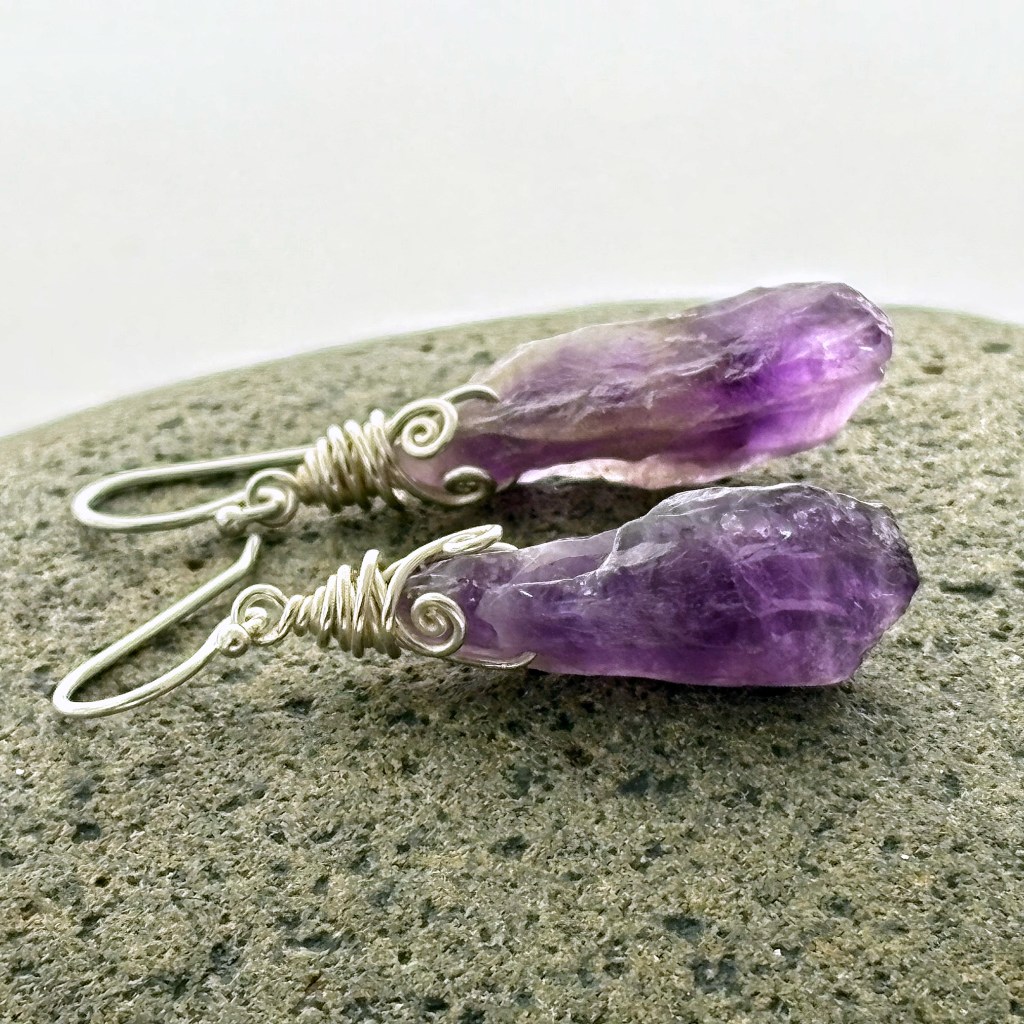 Two matching raw dogtooth shaped amethyst crystals wire-wrapped with sterling silver sitting on a rock.
