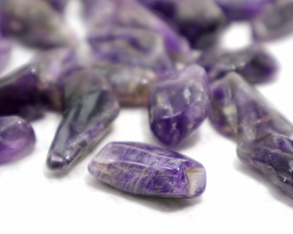 Various tumbled dark purple chevron amethyst crystals on a white background