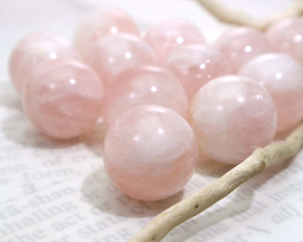 Rose Quartz Crystal Balls on a white surface with a piece of driftwood