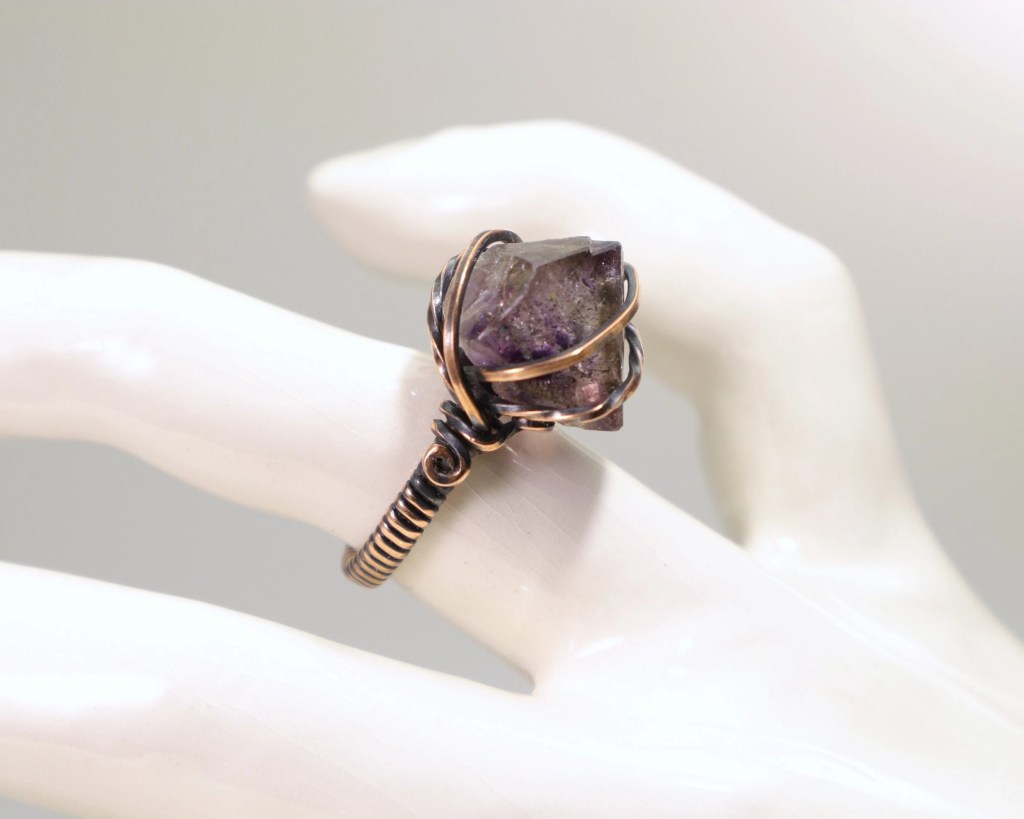 A raw sirius amethyst crystal with goethite inclusions wire-wrapped with copper wire to make a copper ring