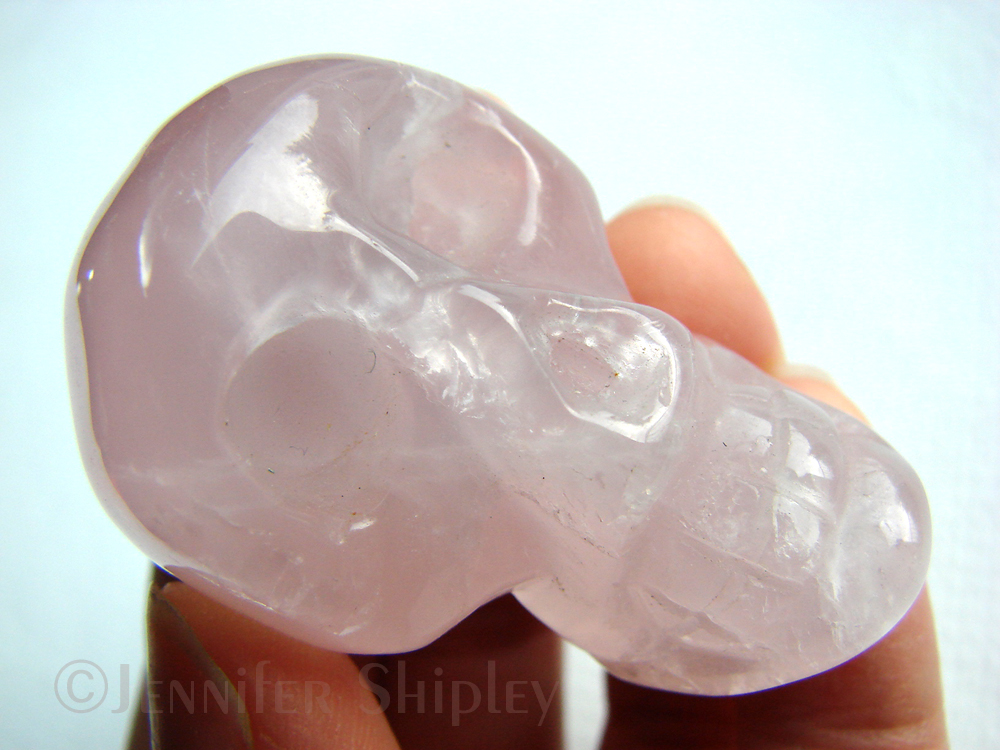 A rose quartz skull held between finger on a neutral background